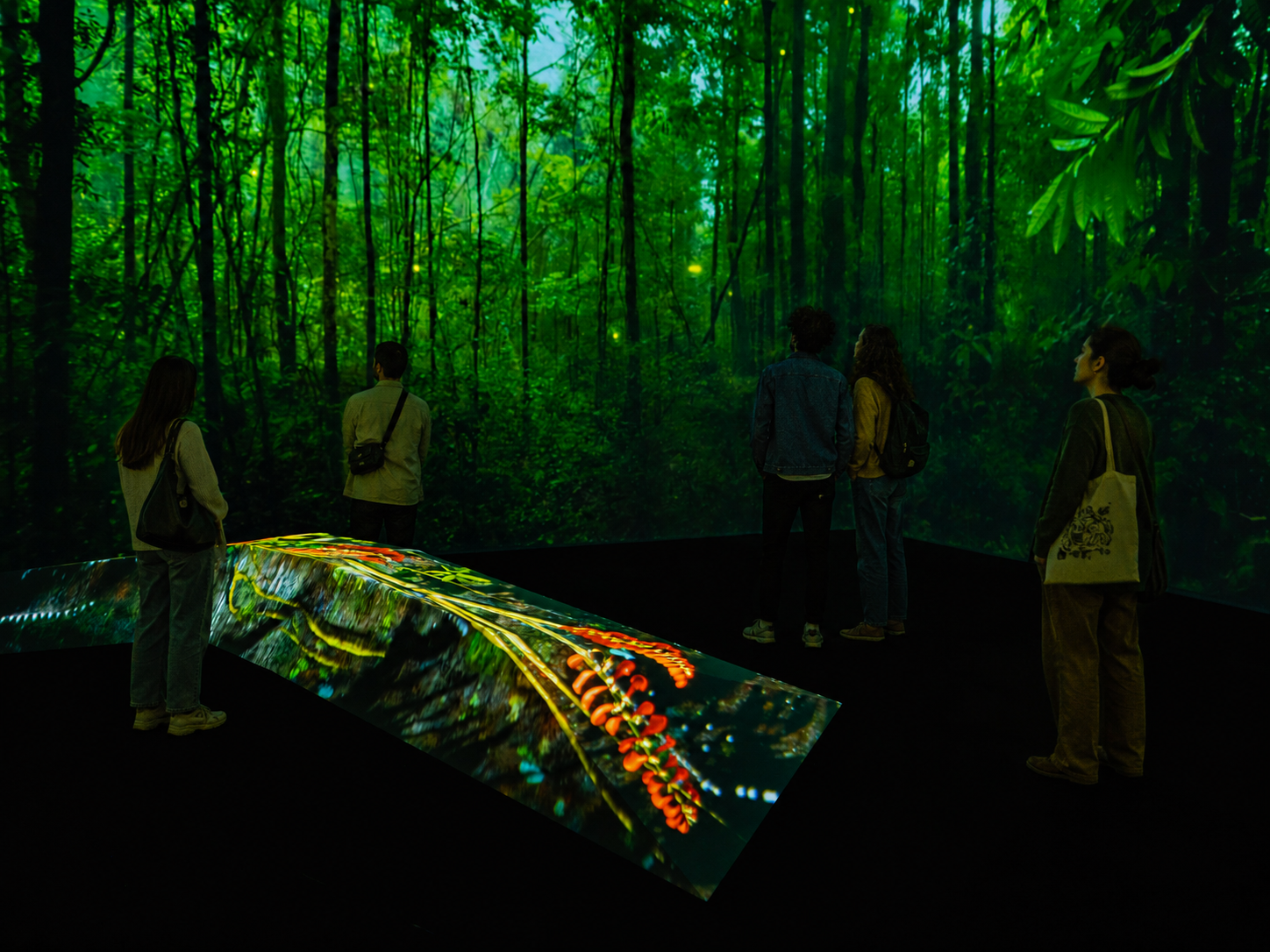 Visitors standing inside a 360-degree rainforest projection, a glowing path of light running across the floor